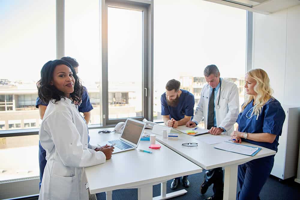 Black female doctor smiling at camera during a meeting with other doctors